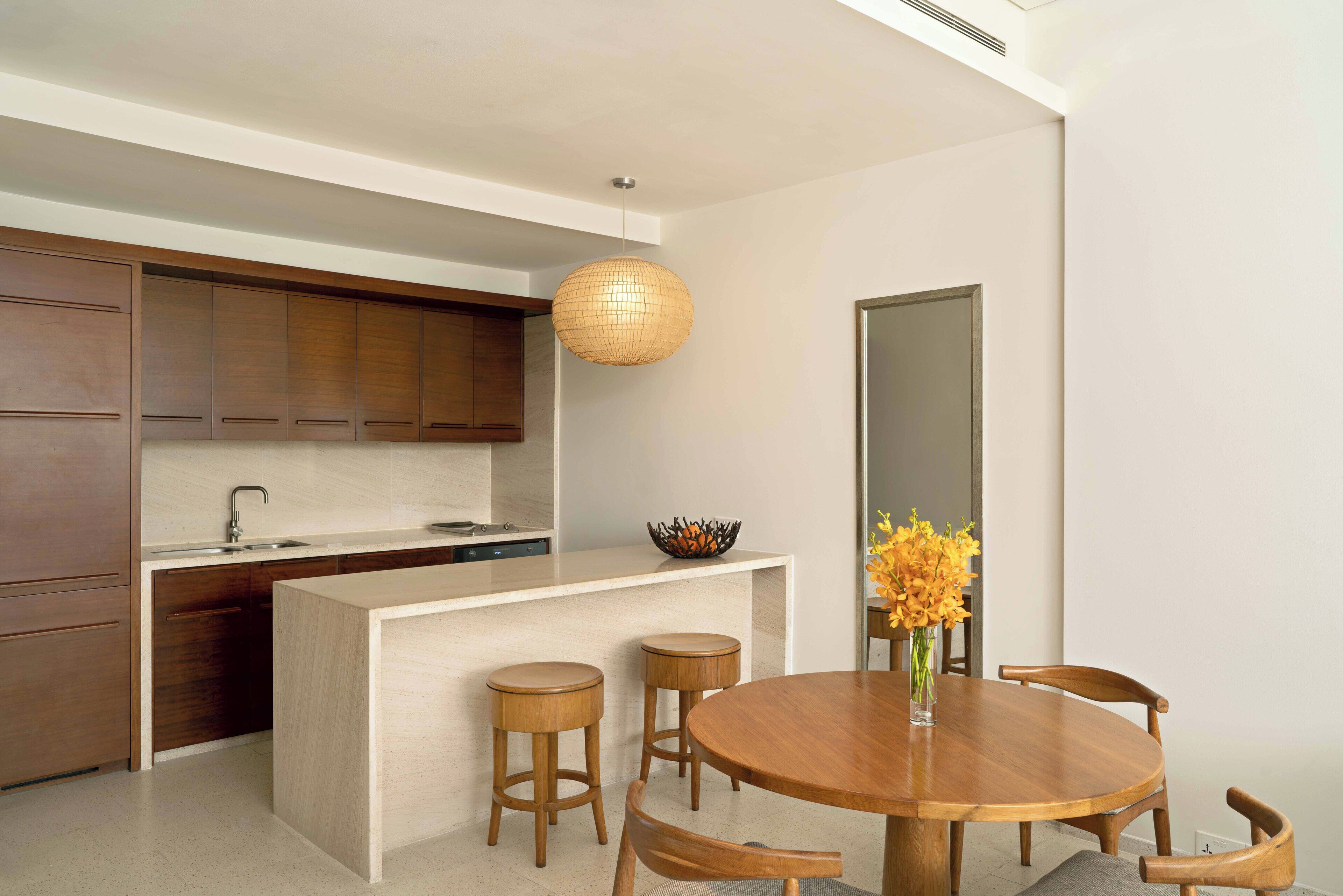 A modern kitchen with wooden cabinets, a white countertop, and a round wooden dining table with stools.