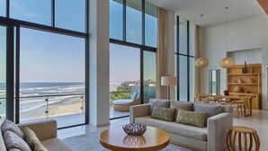 A spacious living room with a large window overlooking a beach, a sofa, a coffee table, and a dining area with a wooden table and chairs. - Hyatt Regency Danang Resort and Spa (Da Nang)