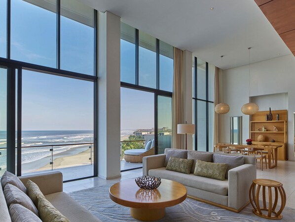 A spacious living room with a large window overlooking a beach, a sofa, a coffee table, and a dining area with a wooden table and chairs. - Hyatt Regency Danang Resort and Spa (Da Nang)