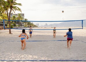 A beach volleyball game with players in swimwear on a sandy court, palm trees, and a clear sky. - Hyatt Regency Danang Resort and Spa (Da Nang)