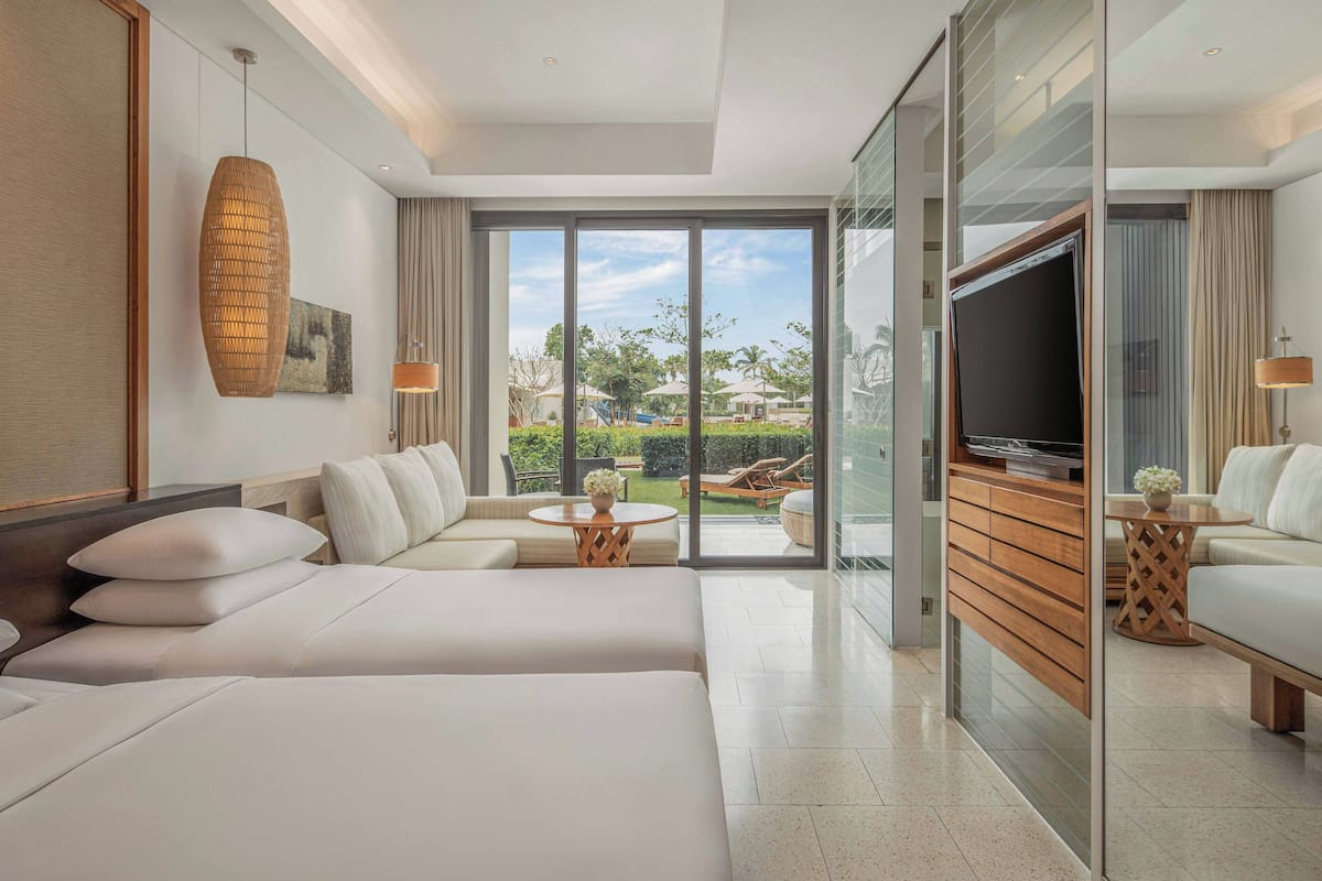 A modern hotel room with a large bed, a sofa, a TV, and a balcony with a view of the outdoors.