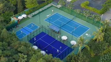 An aerial view of a tennis court complex with multiple courts, seating areas, and surrounding greenery.