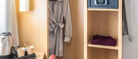 Habitació d'hotel amb escriptori de fusta, una bata penjada a una mànega, minibar i armari amb tancament digital.