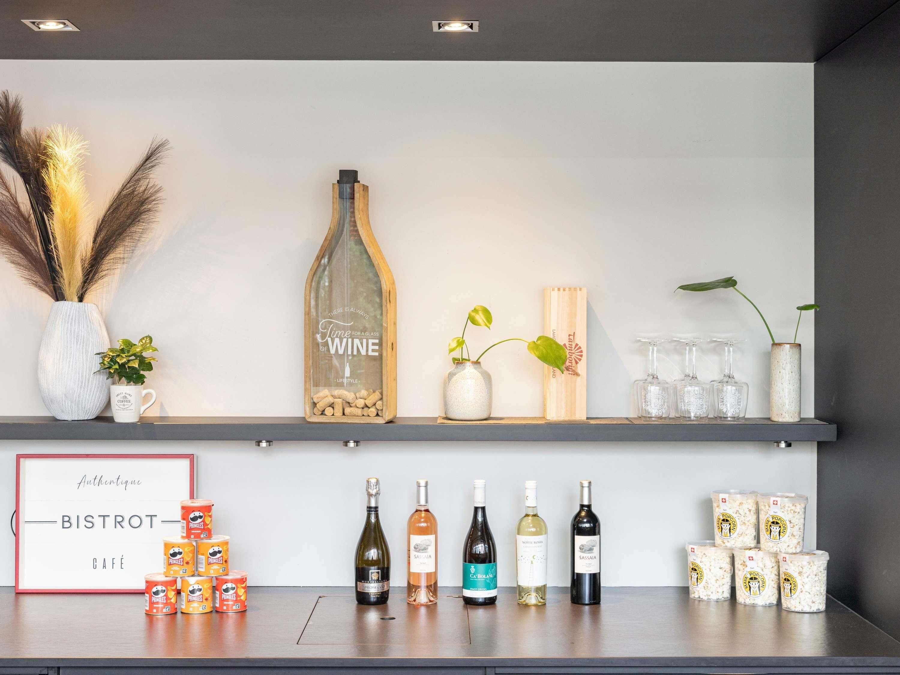 Una presentación de vino y café con botellas y latas, un letrero enmarcado y plantas decorativas.