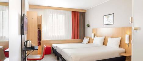 A hotel room with two beds, a desk, a chair, a TV, and a window with curtains.