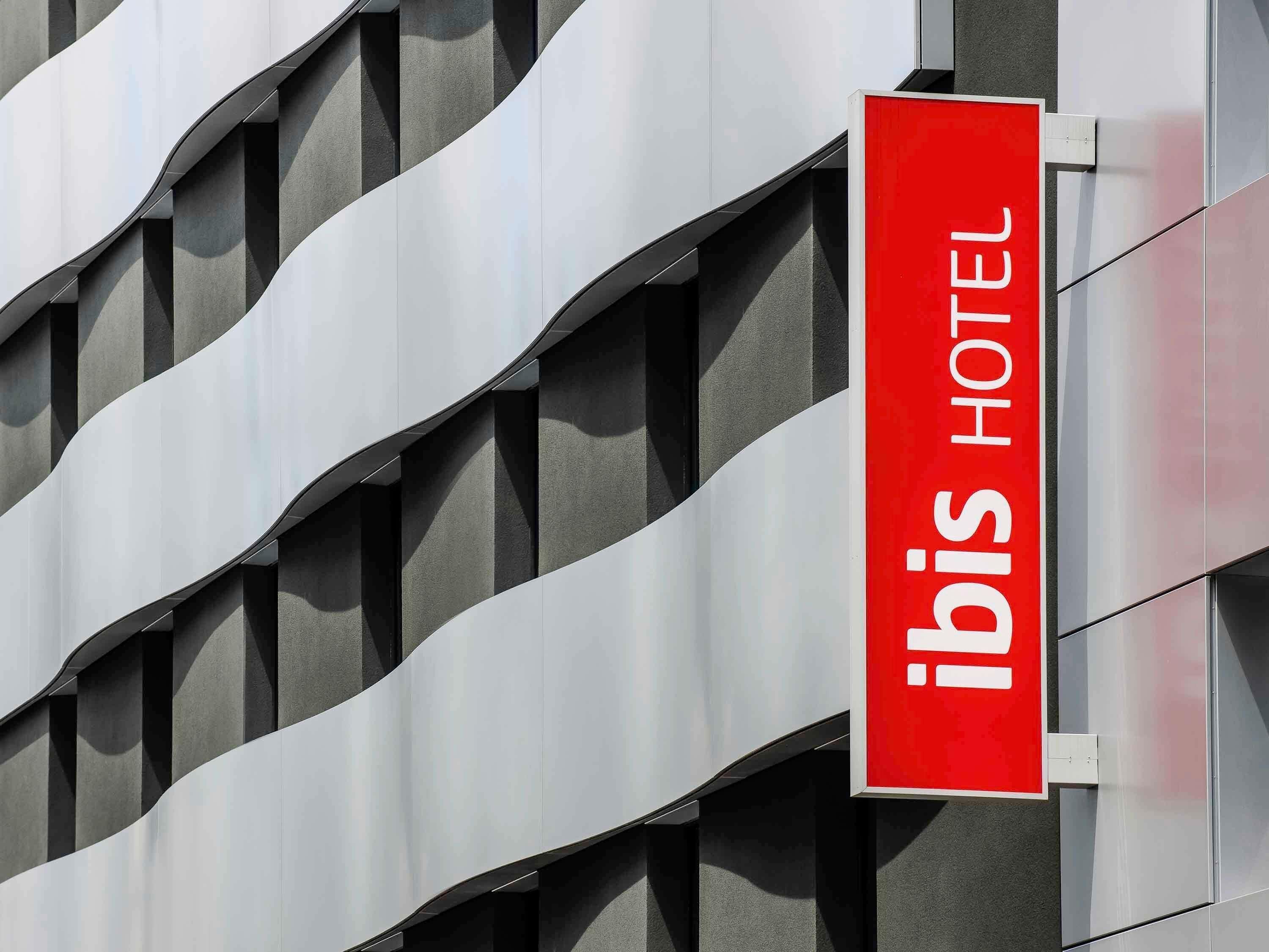 Placa de hotel com o nome 'ibis HOTEL' sobre um fundo vermelho.
