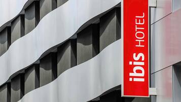 Placa de hotel com o nome 'ibis HOTEL' sobre um fundo vermelho.