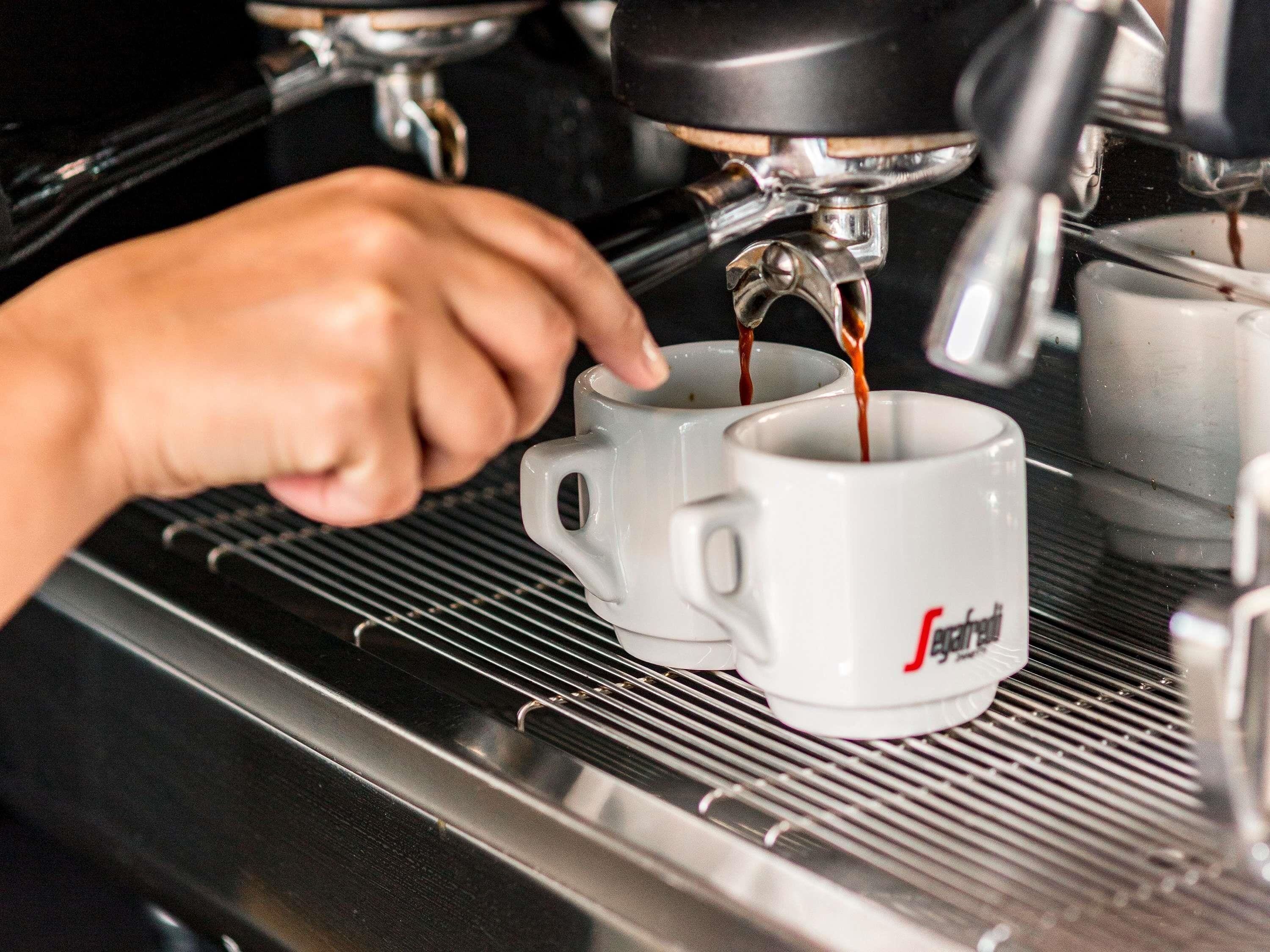 Una mano operando una cafetera, sirviendo café en una taza.