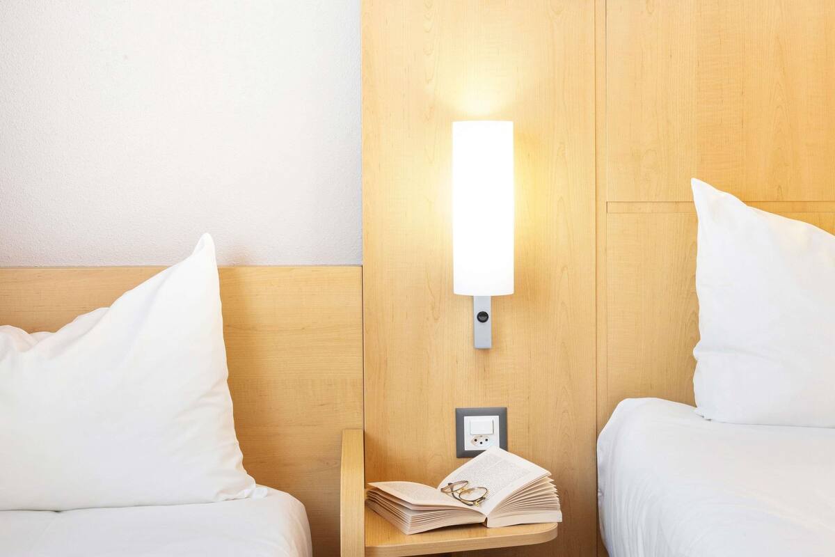 A hotel room with two beds, a nightstand with a lamp, and a wall socket.