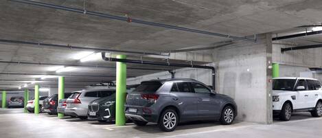 Un aparcamiento de varios niveles con pilares de hormigón y una fila de coches estacionados.