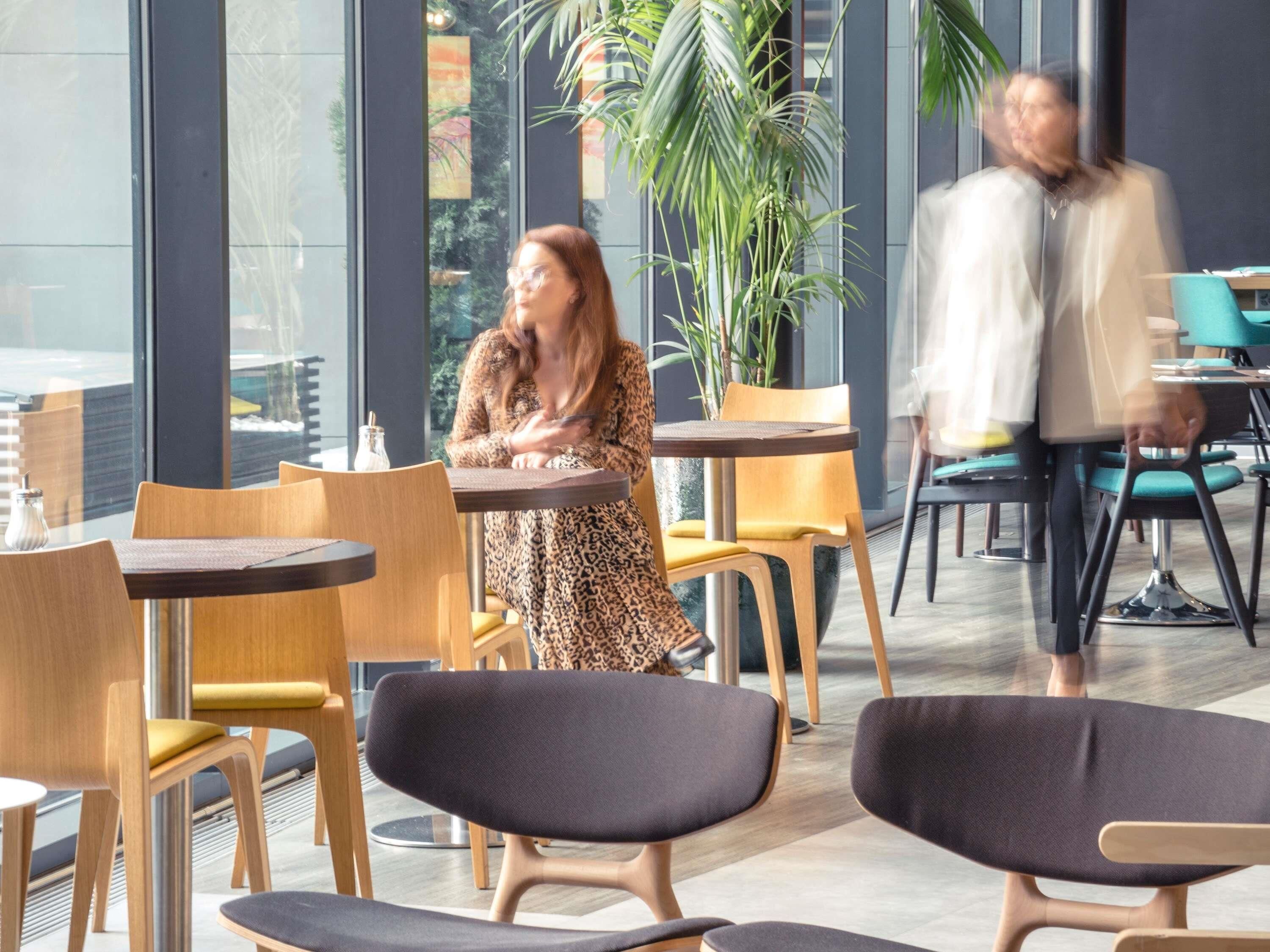 Un espace de détente intérieur moderne, doté de tables et de chaises, de grandes fenêtres et de plantes d’intérieur.