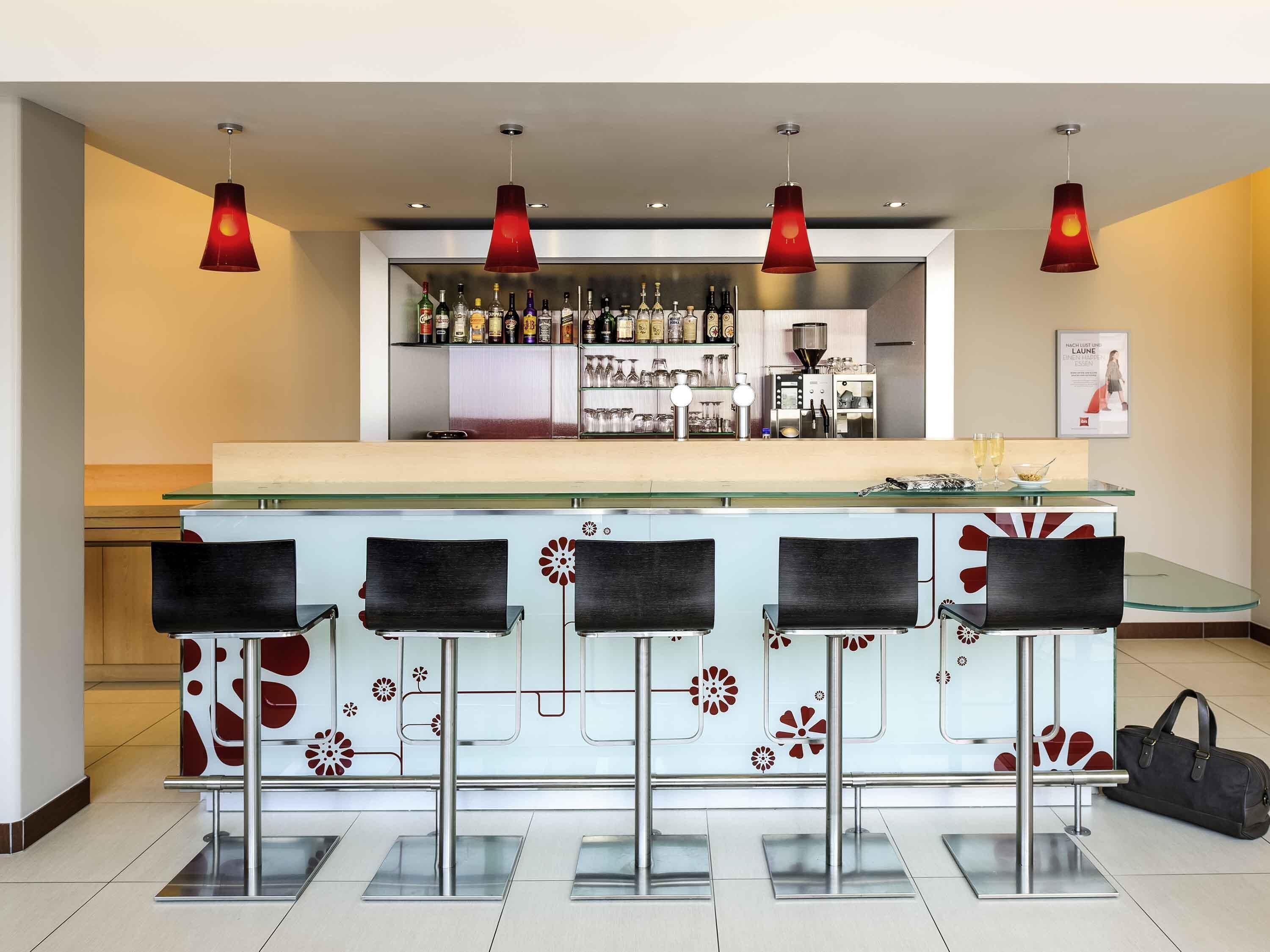 A bar area with a glass counter, black bar stools, and red pendant lighting.