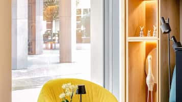Un interior moderno con una silla amarilla, una mesita con un florero y una estantería con adornos.