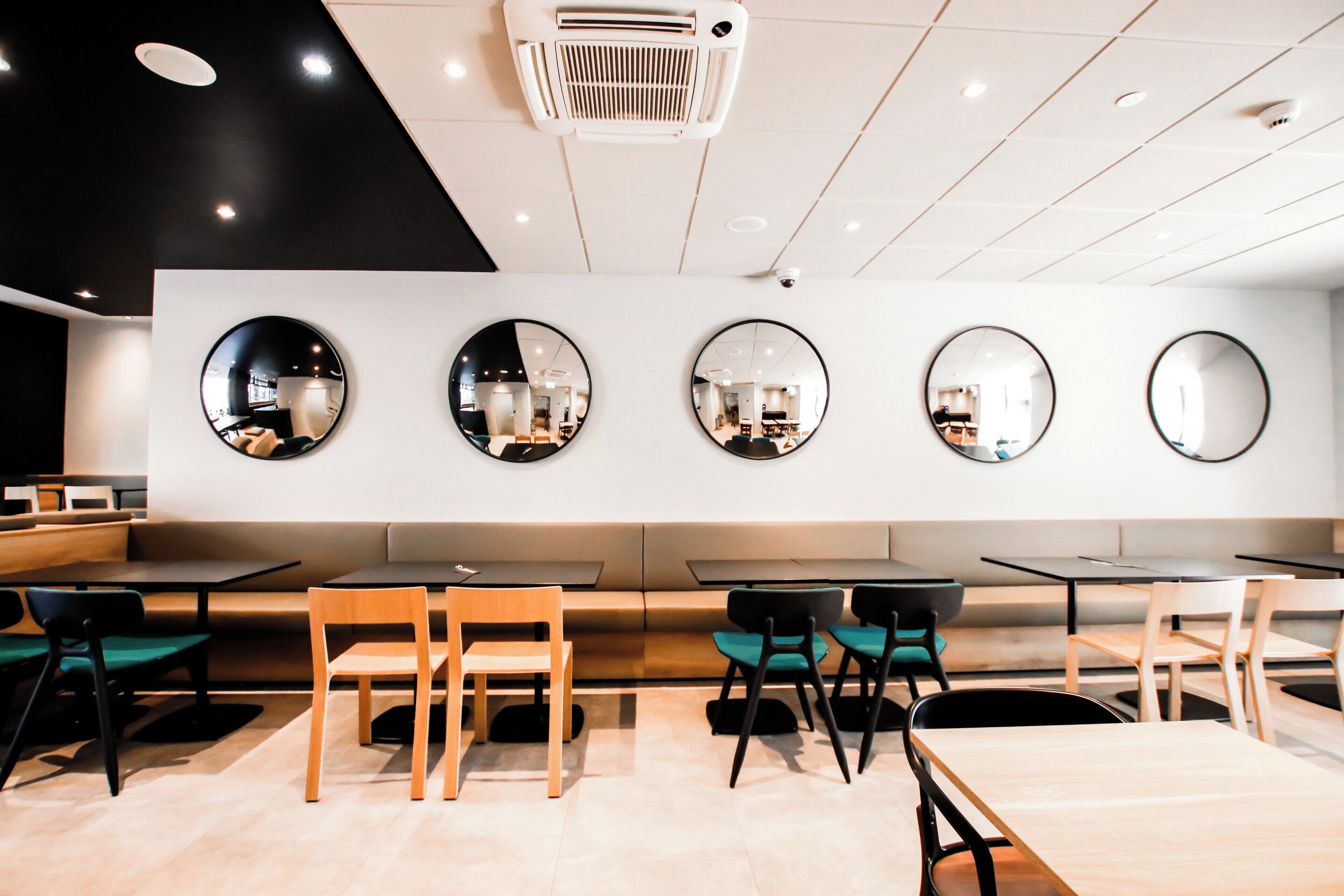 Un ristorante moderno con specchi rotondi alle pareti, tavoli in legno e sedie nere.