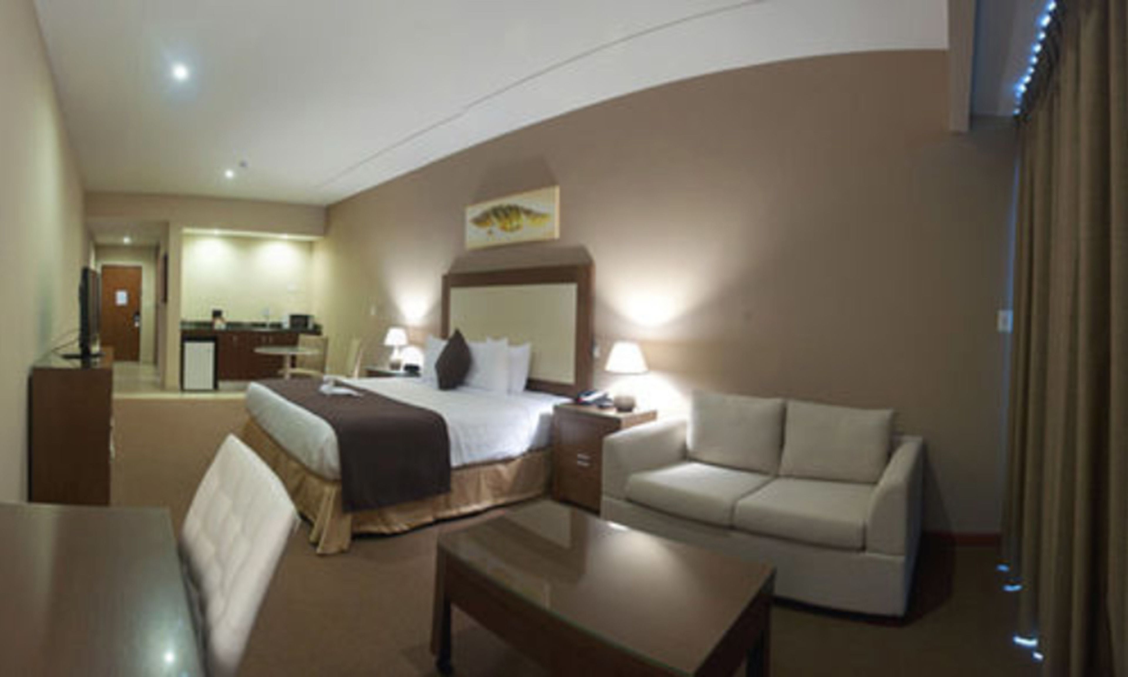 Ein Hotelzimmer mit einem Bett, einem Schreibtisch, einem Sessel, einer Couch und einem Fernseher.