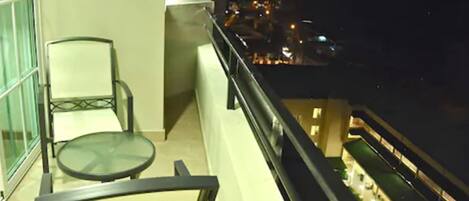 Un balcone con tavolo e sedie in vetro che si affaccia su una vista notturna della città.
