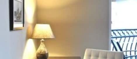 Una habitación con un escritorio de madera oscura, una lámpara, una silla acolchada y cuadros en la pared.