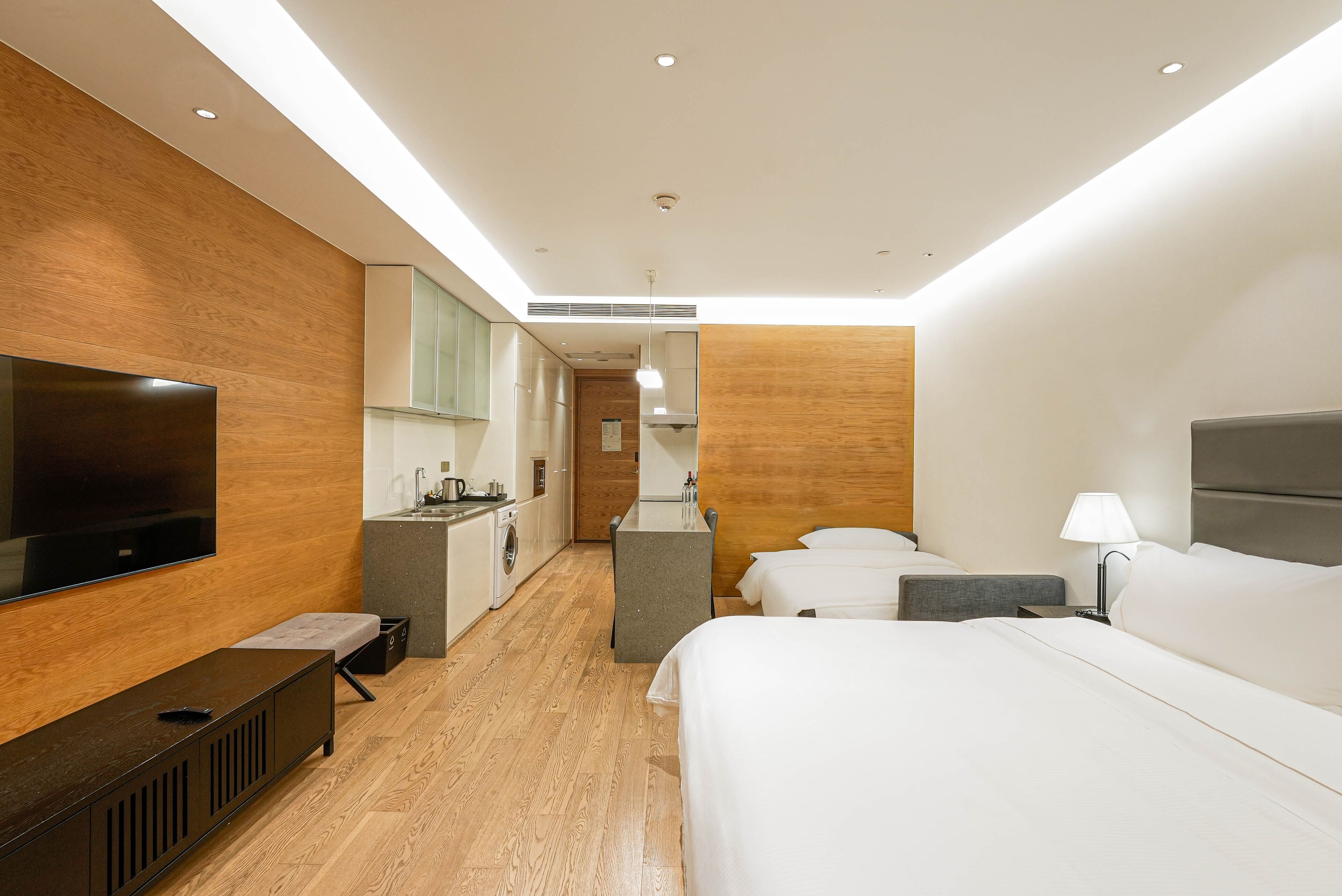 A modern hotel room with a large bed, a TV, a kitchenette, and a bathroom.