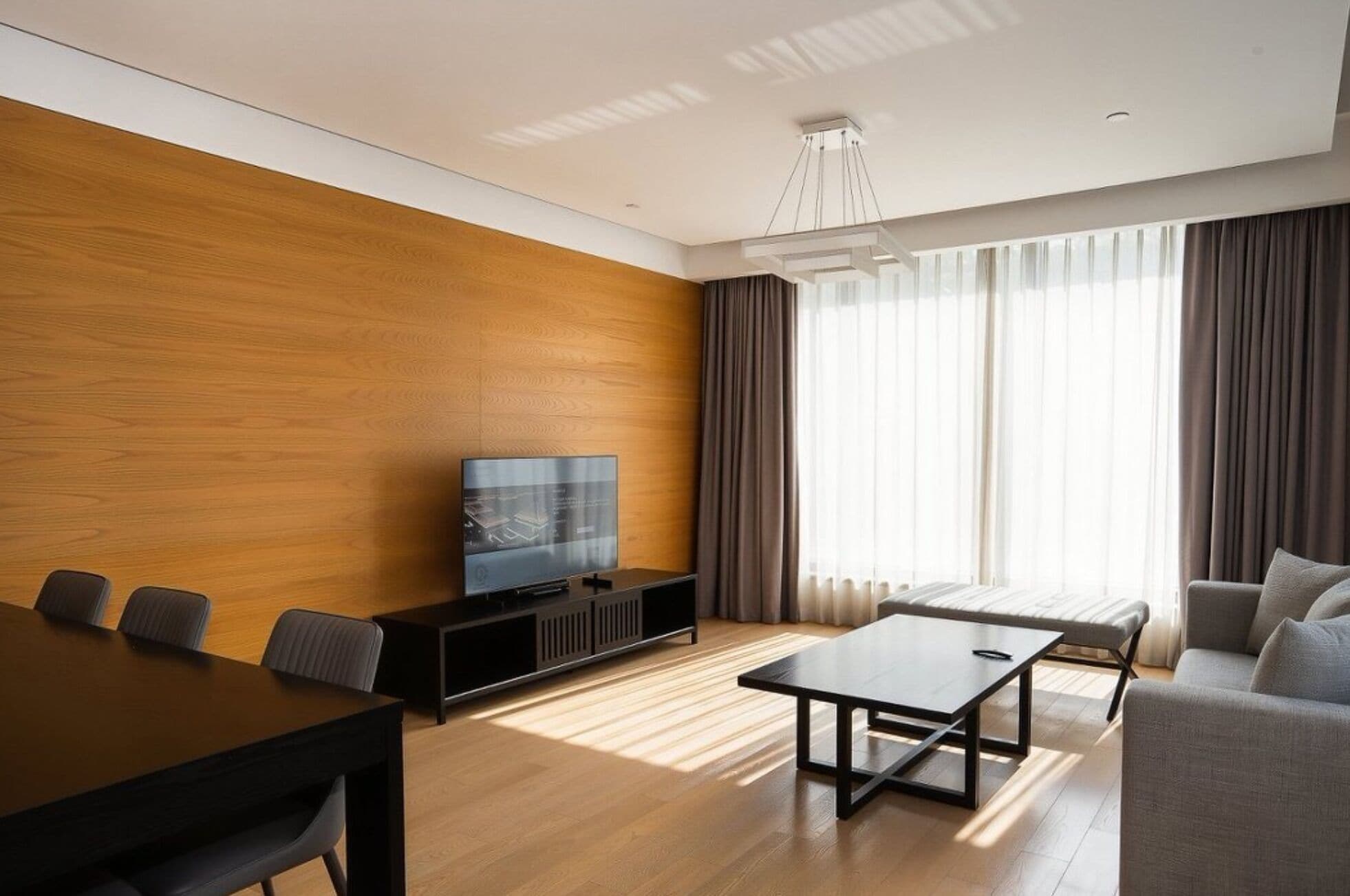 A modern living room with a wooden accent wall, a flat-screen TV, a dining table, and a sofa.