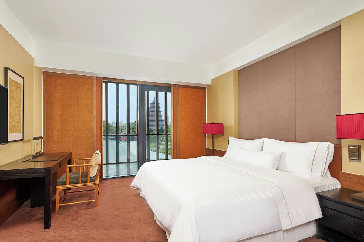 A hotel room with a bed, desk, chair, and a view of a pagoda through a sliding door.