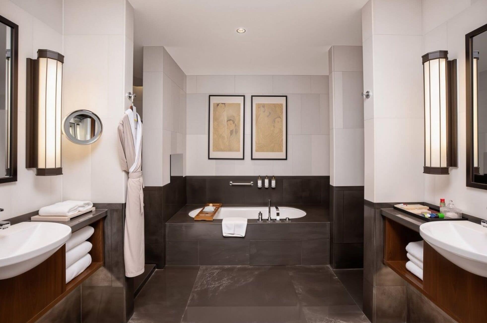 A modern bathroom with two sinks, a bathtub, and two framed artworks on the wall.