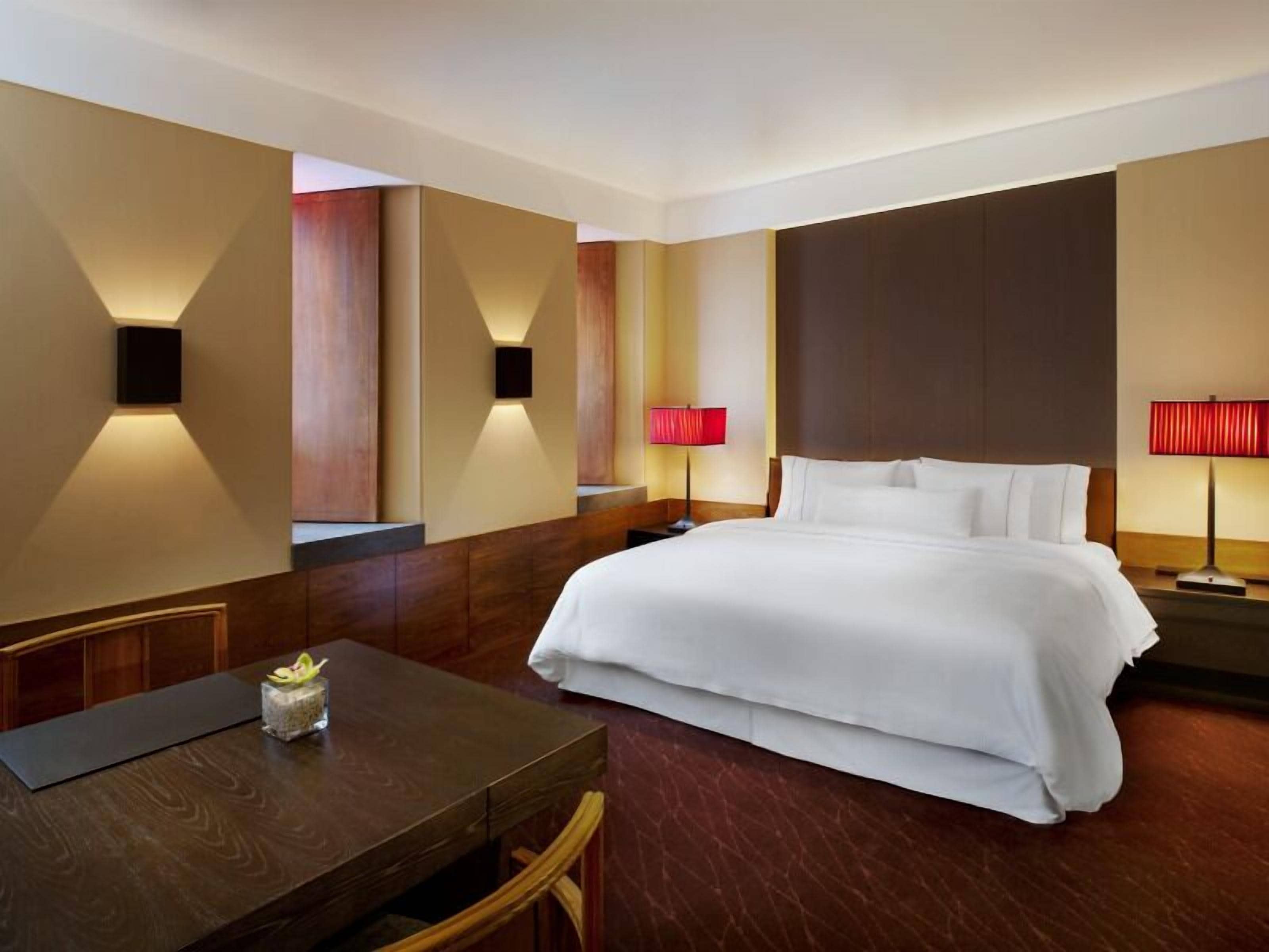 A hotel room with a large bed, two bedside tables with lamps, a wooden desk, and a chair.