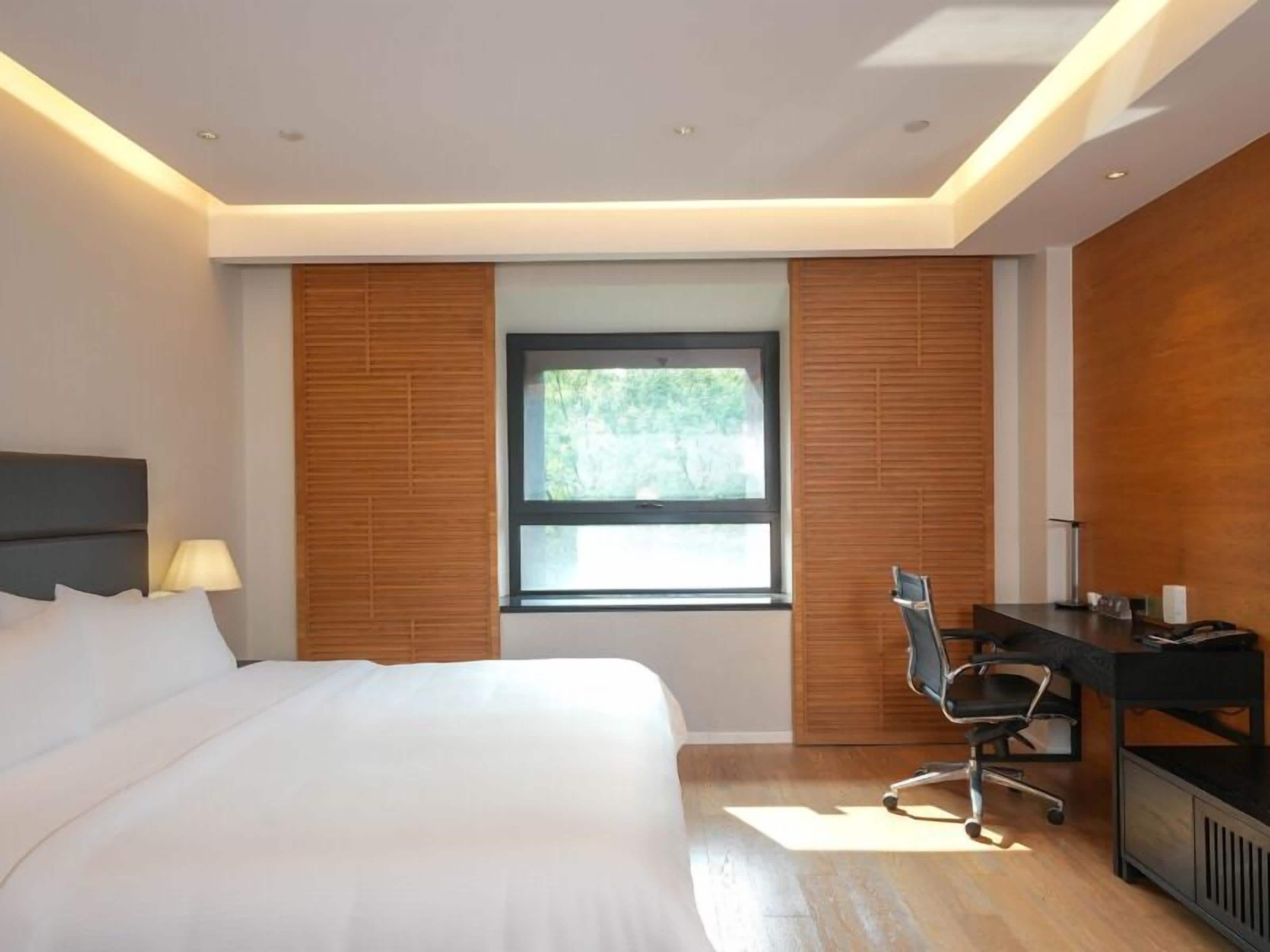 A modern hotel room with a large bed, a desk, and a window with blinds.
