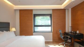 A modern hotel room with a large bed, a desk, and a window with blinds.