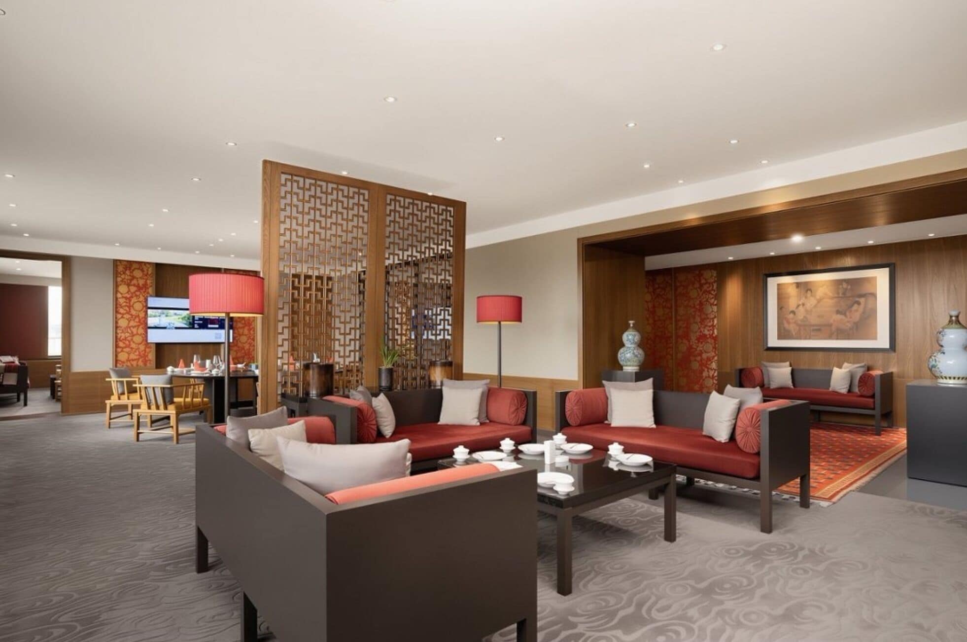 A hotel lobby with seating areas, a dining setup, and a television screen.