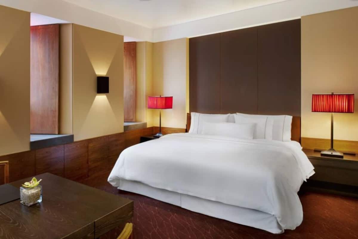 A hotel room with a large bed, a wooden desk, and two wall-mounted lamps.