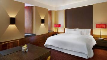 A hotel room with a large bed, a wooden desk, and two wall-mounted lamps.