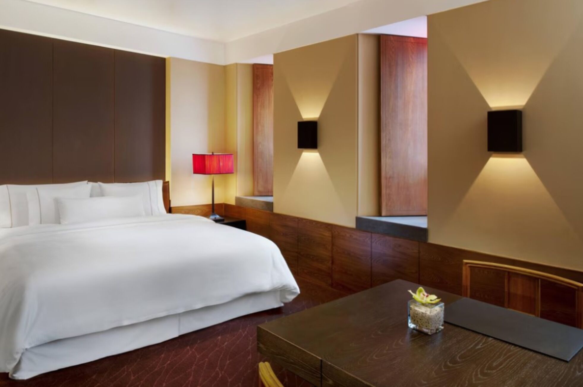 Une chambre d’hôtel avec un grand lit, une table de chevet avec une lampe et une petite table ornée d’un objet décoratif.