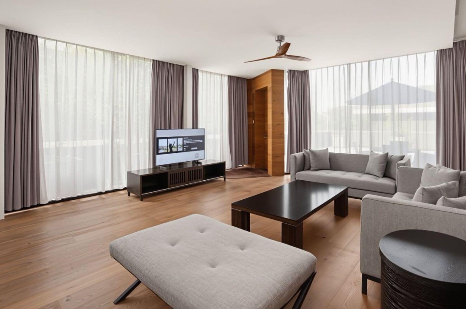 A modern living room with a flat-screen TV, a sofa, a coffee table, and a ceiling fan.