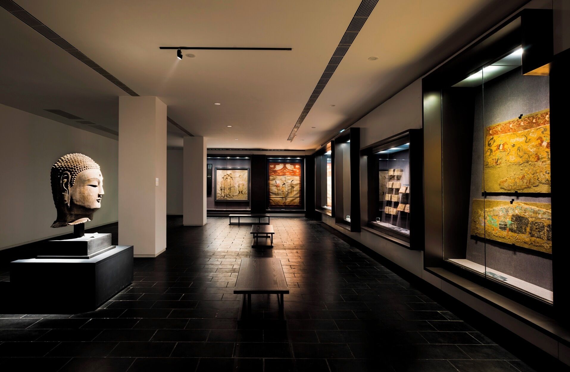 A modern interior with a long hallway, a Buddha statue, and framed artwork on the walls.