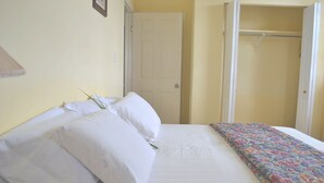 Una cama bien hecha con sábanas blancas y una colcha colorida, una puerta cerrada y un armario con barra.