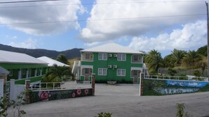 Un edificio verde con techo blanco, rodeado de palmeras y un paisaje montañoso.