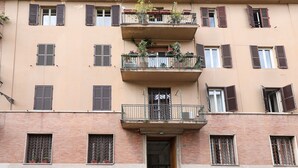 A multi-story building with balconies, windows with shutters, and potted plants. - Maison Colosseo (Rome)