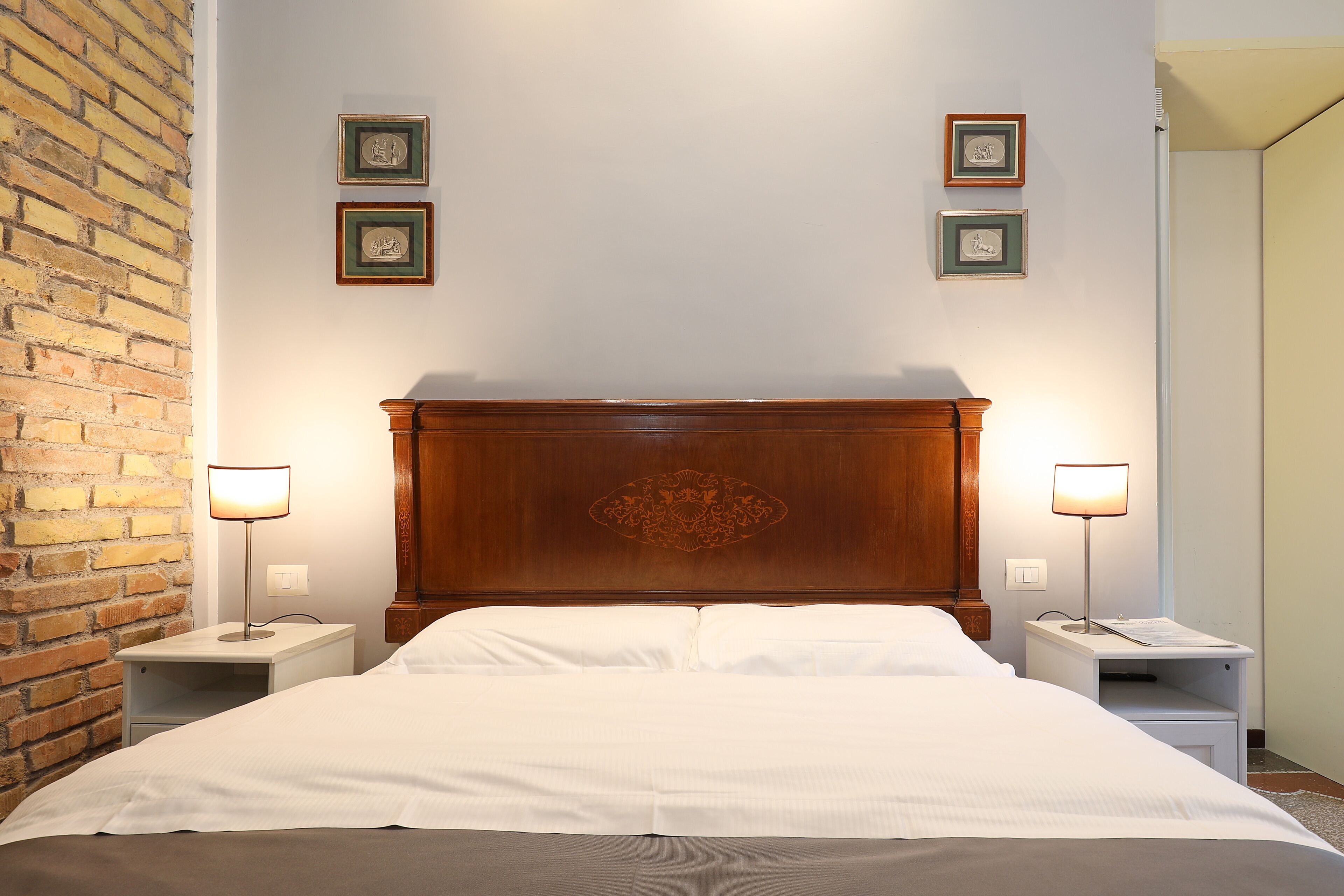 A neatly made bed with a wooden headboard, two bedside tables with lamps, and framed pictures on the wall.