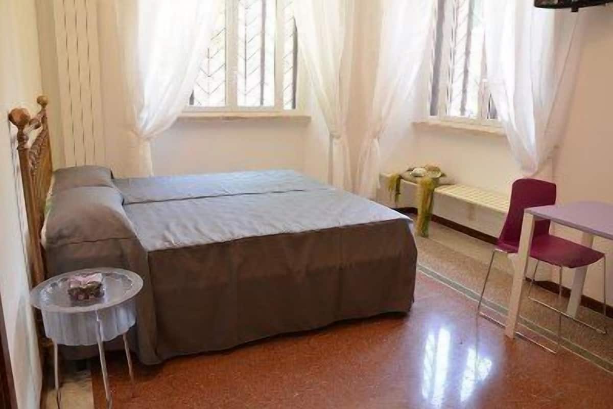 A room with a bed, a small table, a chair, and a window with curtains.