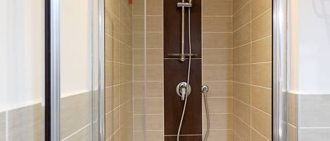 A glass-enclosed shower stall with a handheld showerhead and a wall-mounted faucet.