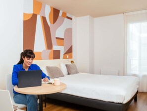 Une chambre d’hôtel moderne avec un lit, un ordinateur portable posé sur une petite table et une grande œuvre d’art abstraite accrochée au mur.