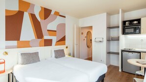 Een moderne hotelkamer met een groot bed, een kitchenette en een badkamer door een open deur zichtbaar.