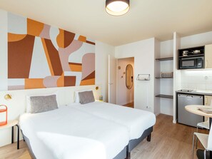 Een moderne hotelkamer met een groot bed, een kitchenette en een badkamer door een open deur zichtbaar.