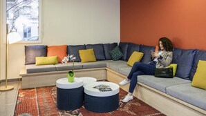 Een moderne wachtruimte met een hoekbank, ronde salontafels en een kamerbreed tapijt met een patroon.