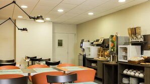 Een eetruimte met tafels, stoelen, een koffieapparaat en een koelkast.