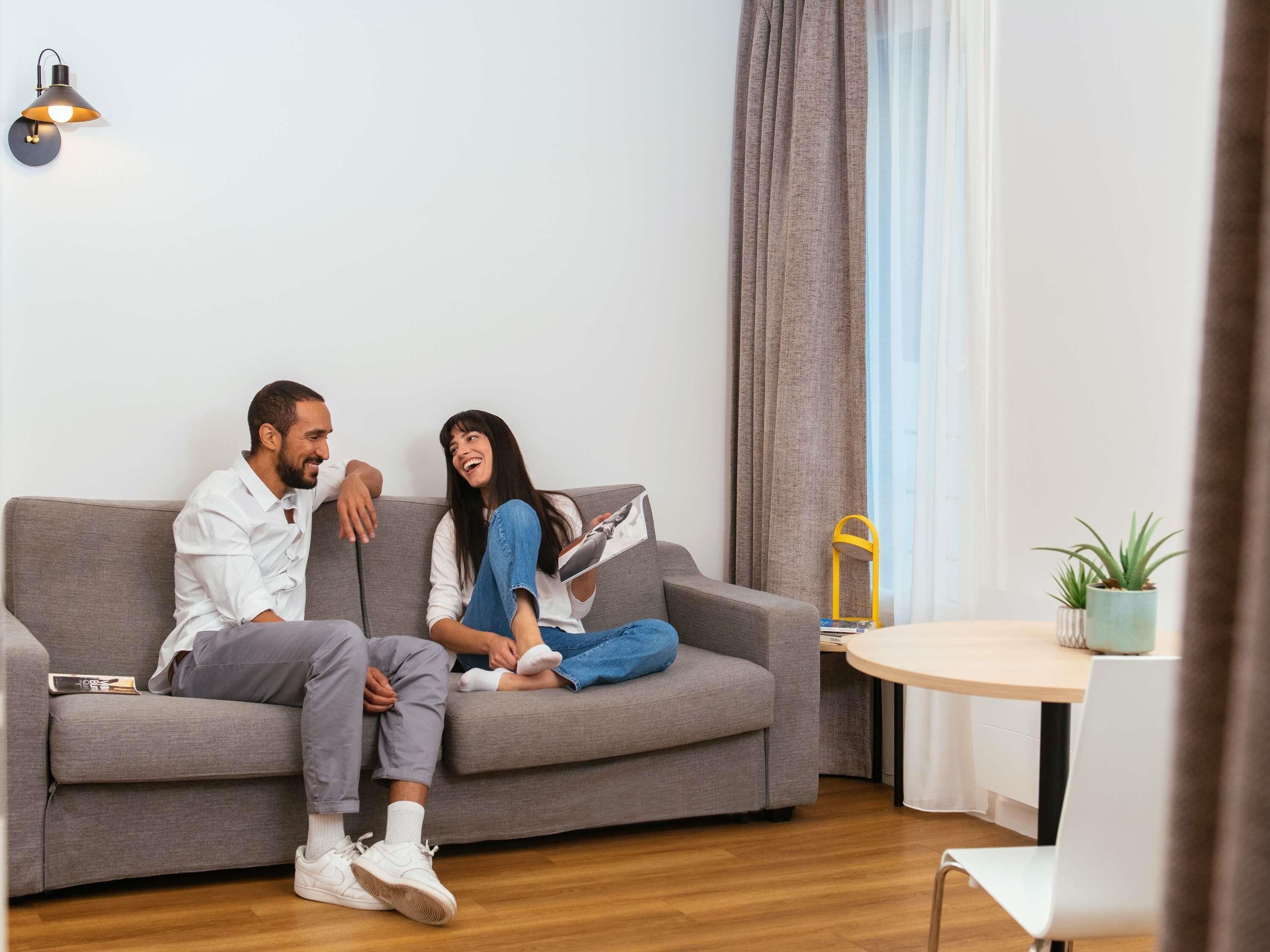 Una sala de estar moderna con un sofá gris, una mesita redonda con una planta en maceta y una lámpara de pie amarilla.