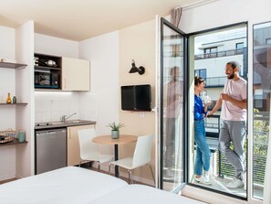 Una cocina moderna con microondas, pileta y armarios. Hay una zona de comedor con una mesa y sillas, y una pequeña planta en maceta. Un televisor está montado en la pared.