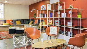 Een bibliotheek met een rode muur, witte boekenplanken en oranje stoelen.