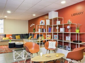 Een bibliotheek met een rode muur, witte boekenplanken en oranje stoelen.