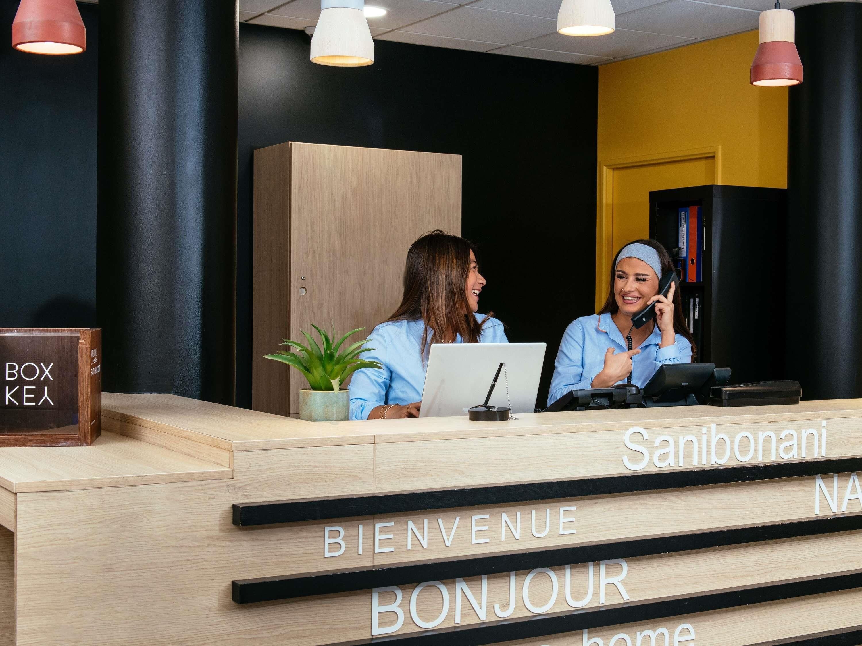 Un comptoir d’accueil avec un revêtement en bois, une plante en pot et une pancarte sur laquelle on peut lire : « BIENVENUE, BONJOUR ».
